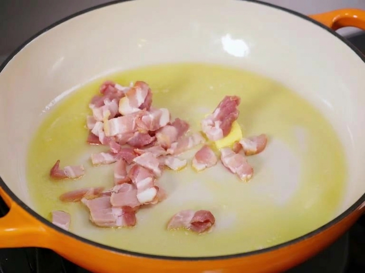 Gewürfelter Speck brutzelt in einer Pfanne mit Butter und Öl.