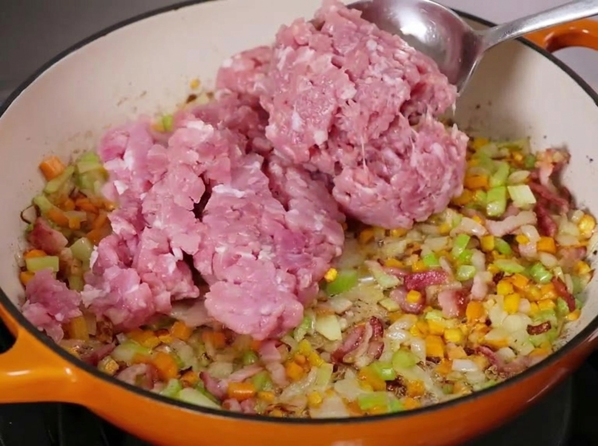 Ein großer Löffel rohes Hackfleisch wird in die Pfanne gegeben.