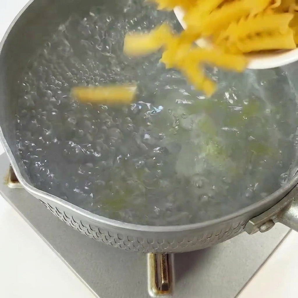 Trockene Fusilli-Nudeln werden aus einer kleinen Schale in einen Topf mit kochendem Wasser gegossen.