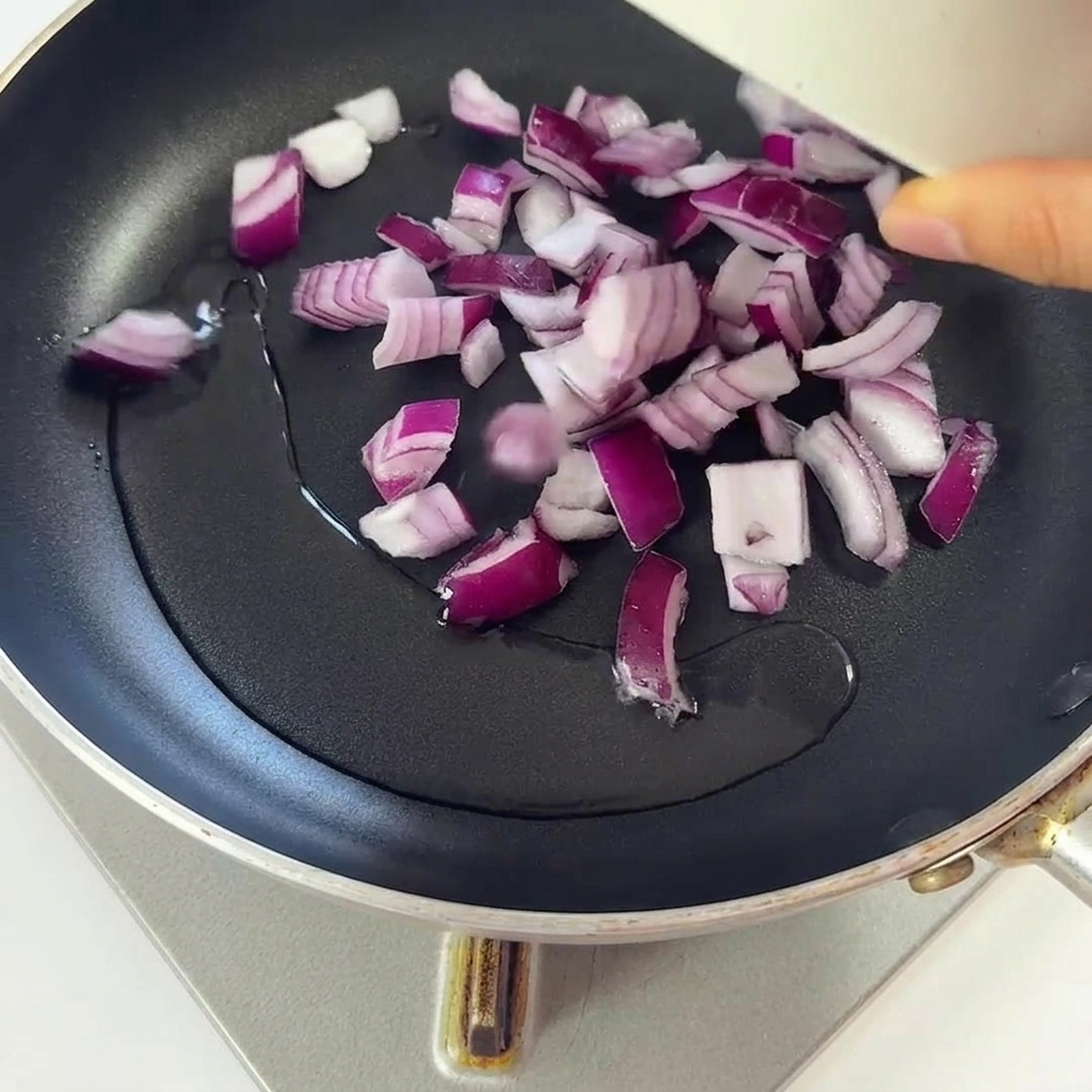 Gehackte rote Zwiebeln braten in einer Pfanne mit schimmerndem, heißem Öl.
