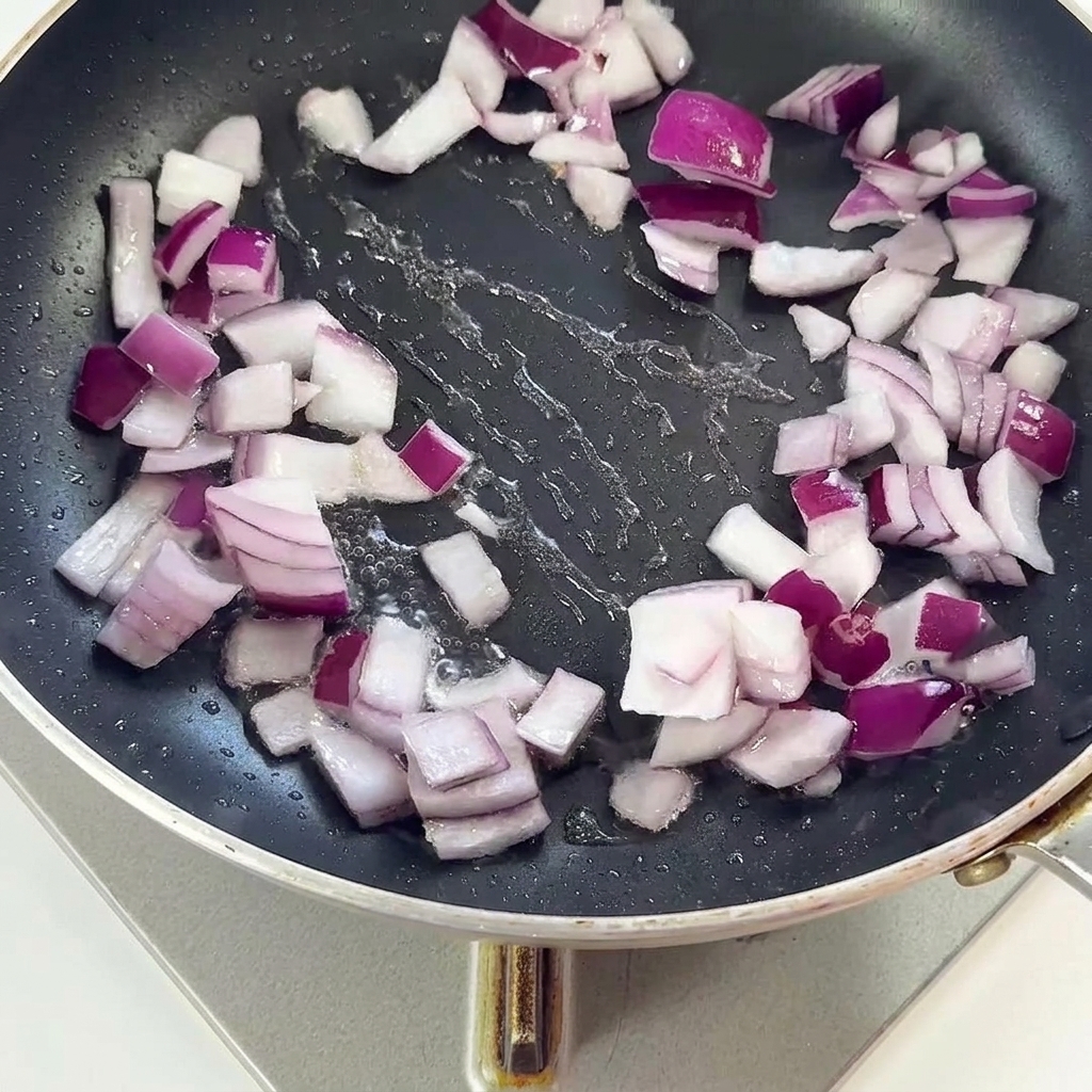 Speckstücke und rote Zwiebeln werden zusammen in einer schwarzen Bratpfanne angebraten.