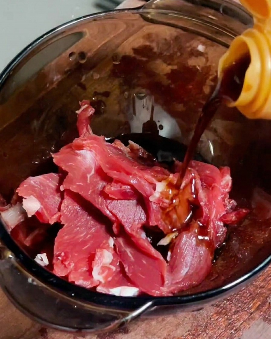 Sojasauce wird in einer Glasschüssel über frische, dünne Rindfleischstreifen gegossen.