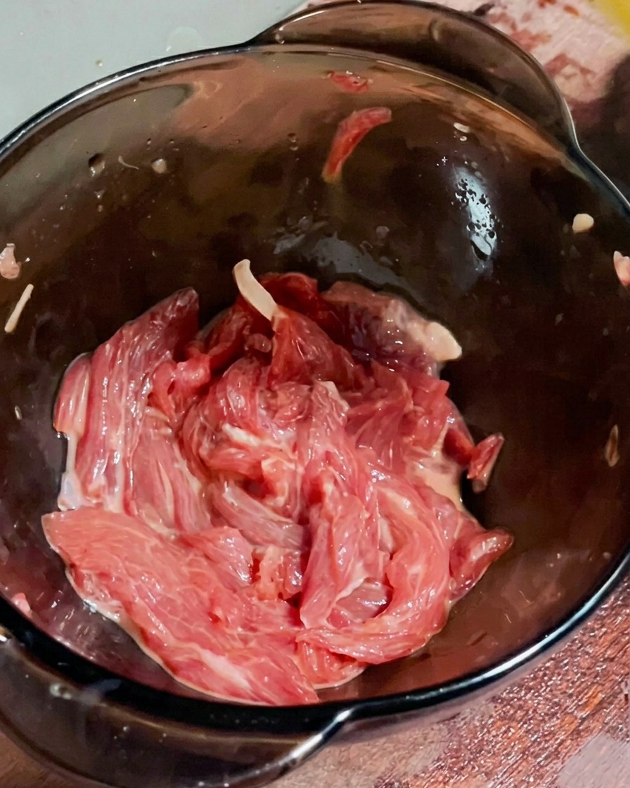 Ein Spritzer Öl wird über das marinierte Rindfleisch gegeben.