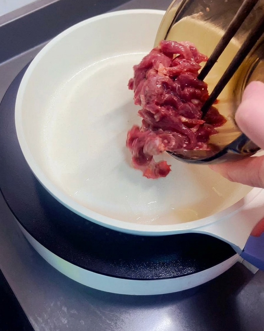 Mariniertes Rindfleisch wird aus der Glasschüssel in eine heiße, weiße Pfanne gegeben.