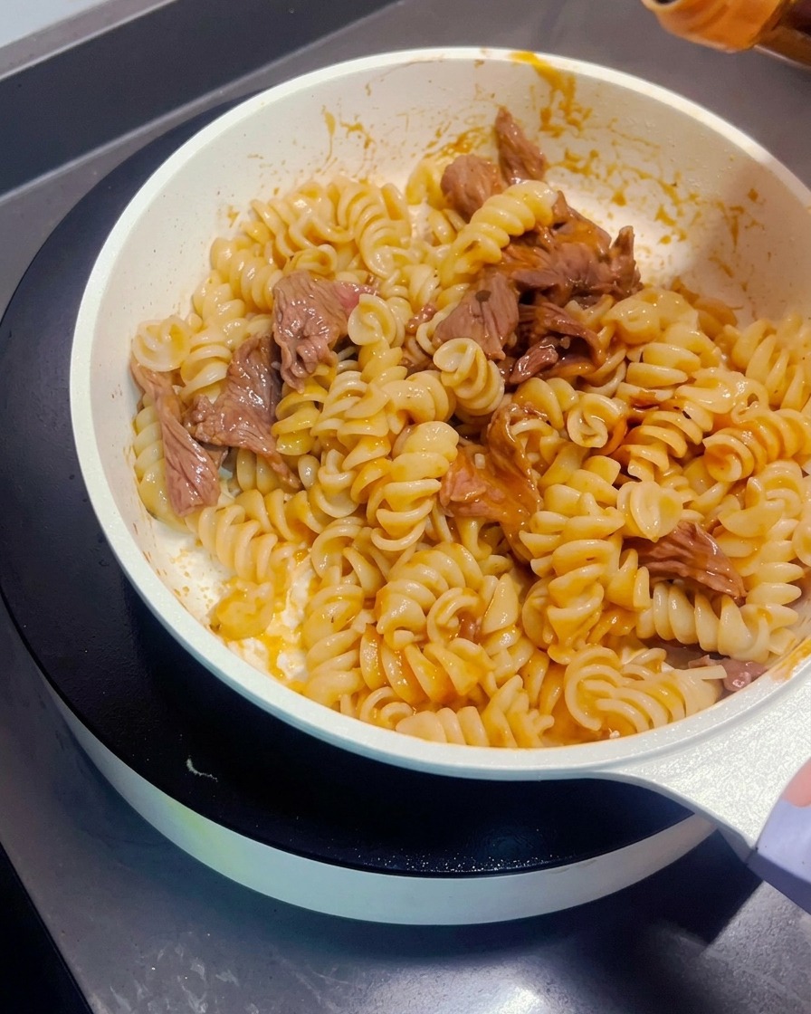 Dunkle Sojasauce wird über die gebratenen Nudeln und das Fleisch geträufelt.