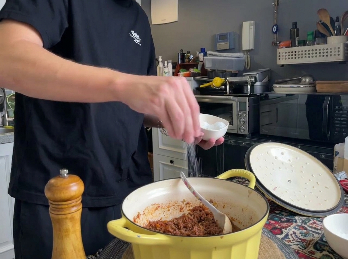 Frisch gemahlener schwarzer Pfeffer und Salz werden in einen Topf mit fertigem Fleischragù gestreut.