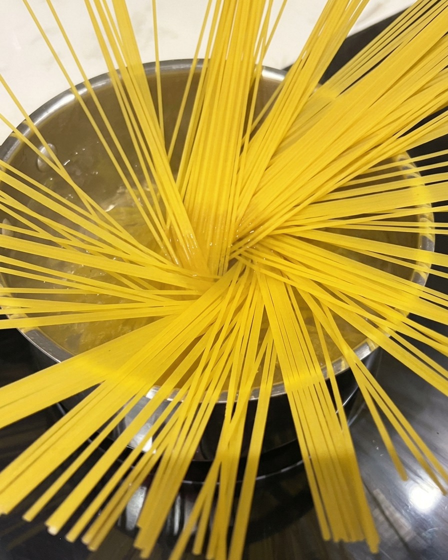 Spaghetti kochen in einem großen Topf mit kochendem Wasser, Dampf steigt auf.