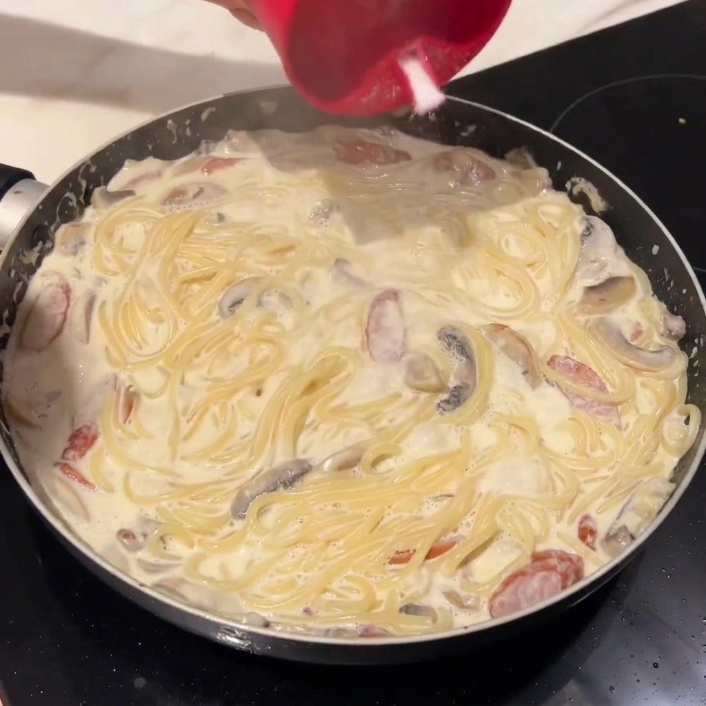 Gekochte Spaghetti werden in die Pfanne mit der cremigen Soße gegeben.