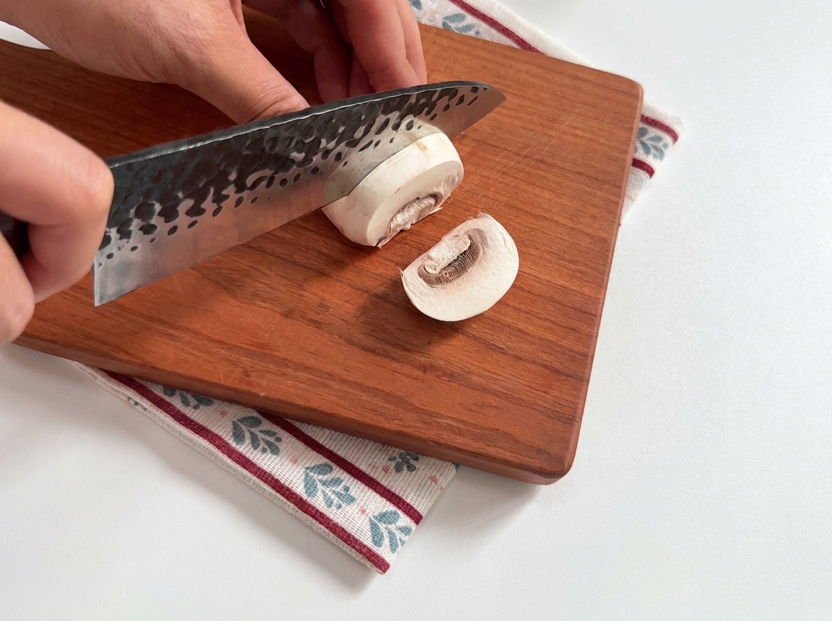 Frische weiße Champignons, die auf einem Holzbrett in Scheiben geschnitten werden.