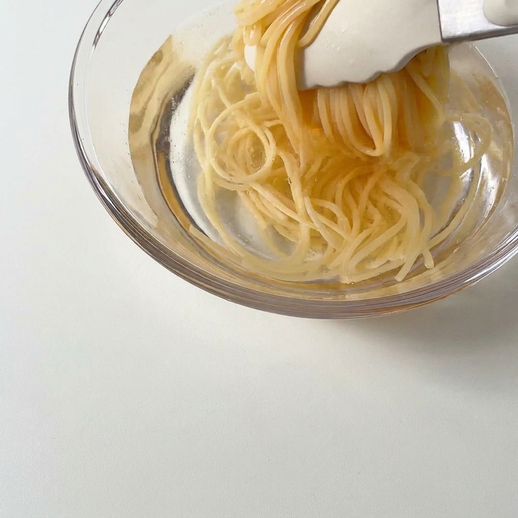 Gekochte Spaghetti werden mit einer Zange in eine Schüssel mit kaltem Wasser gegeben.