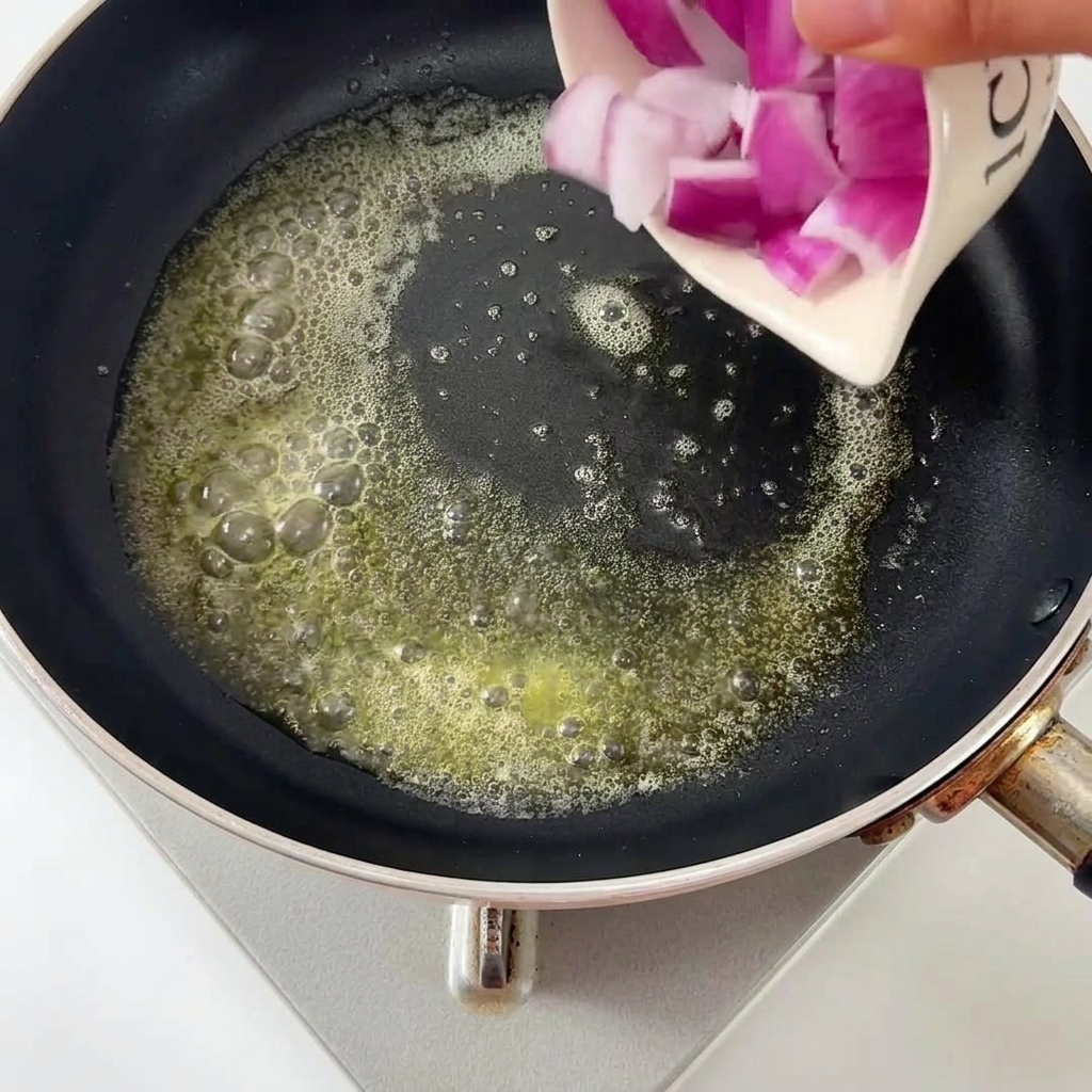 Gehackte Zwiebelwürfel werden in die geschmolzene Butter in der Pfanne gegeben.
