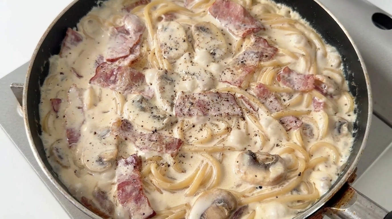 Frisch zubereitete cremige Pilz-Speck-Spaghetti, überzogen mit einer reichhaltigen Sauce und frisch gemahlenem schwarzem Pfeffer.