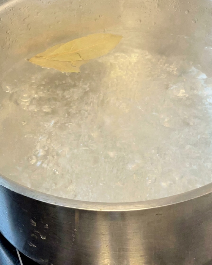 Pasta kocht in einem Topf mit kochendem Wasser und zwei schwimmenden Lorbeerblättern.