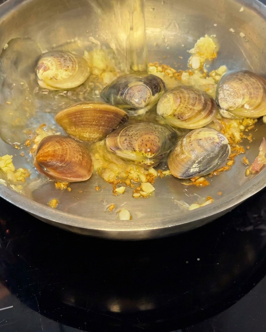 Weißwein wird über die Muscheln in die Pfanne gegossen, um Dampf zu erzeugen.