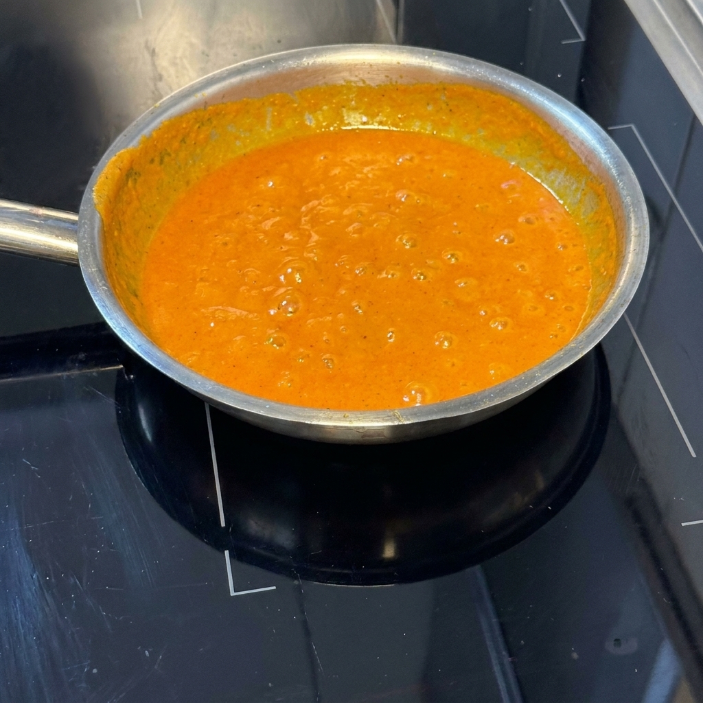 Gekochte Nudeln werden in der lebhaft orangefarbenen Paprikasauce geschwenkt.