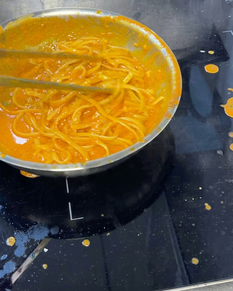 Cremige Pasta in der Pfanne wird mit einem Löffel untergerührt.