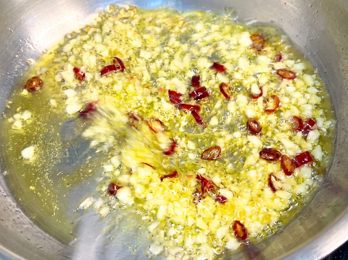 Pasta wird in einer Pfanne mit goldenem Knoblauch und Chiliflocken geschwenkt und mit einer glänzenden Sauce überzogen.