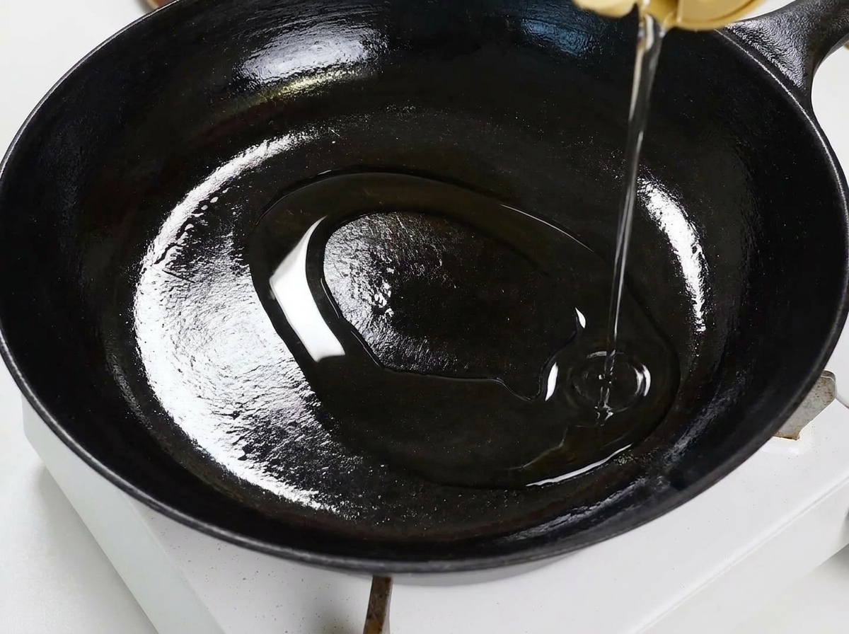 Knoblauchscheiben und Chiliflocken brutzeln in Öl in einer flachen schwarzen Pfanne und werden mit einem Holzspatel gerührt.