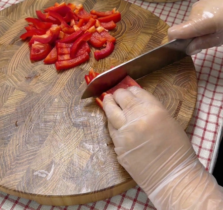 Gewürfelte rote Paprikastücke auf einem Holzschneidebrett.