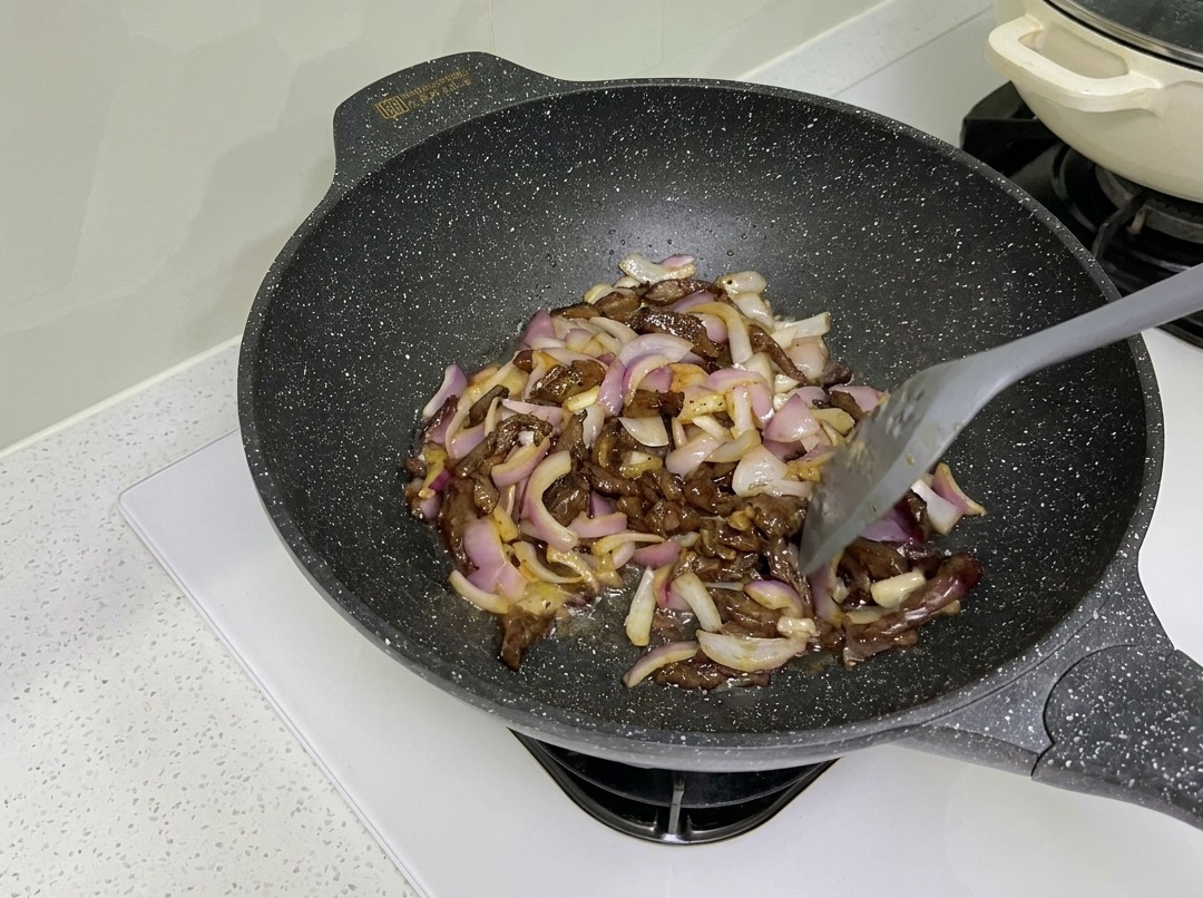Rindfleischstreifen und rote Zwiebeln im Wok angebraten.