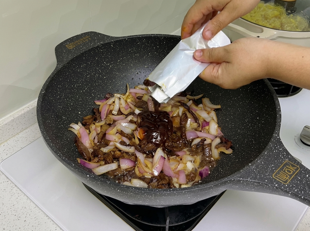 Dunkle Pastasauce und Tomatenmark werden in den Wok zu Fleisch und Zwiebeln gerührt.