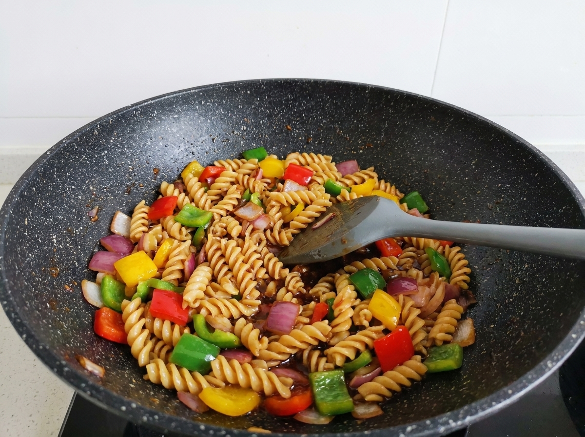 Fusilli, Rindfleisch und bunter Paprika werden mit einem Spatel im Wok geschwenkt und glänzen in der dunklen Sauce.