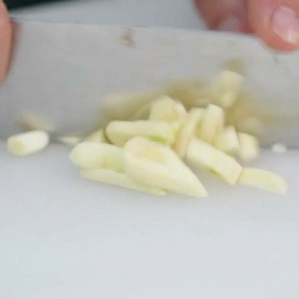 Frische Knoblauchzehen werden auf einem Schneidebrett fein gehackt.