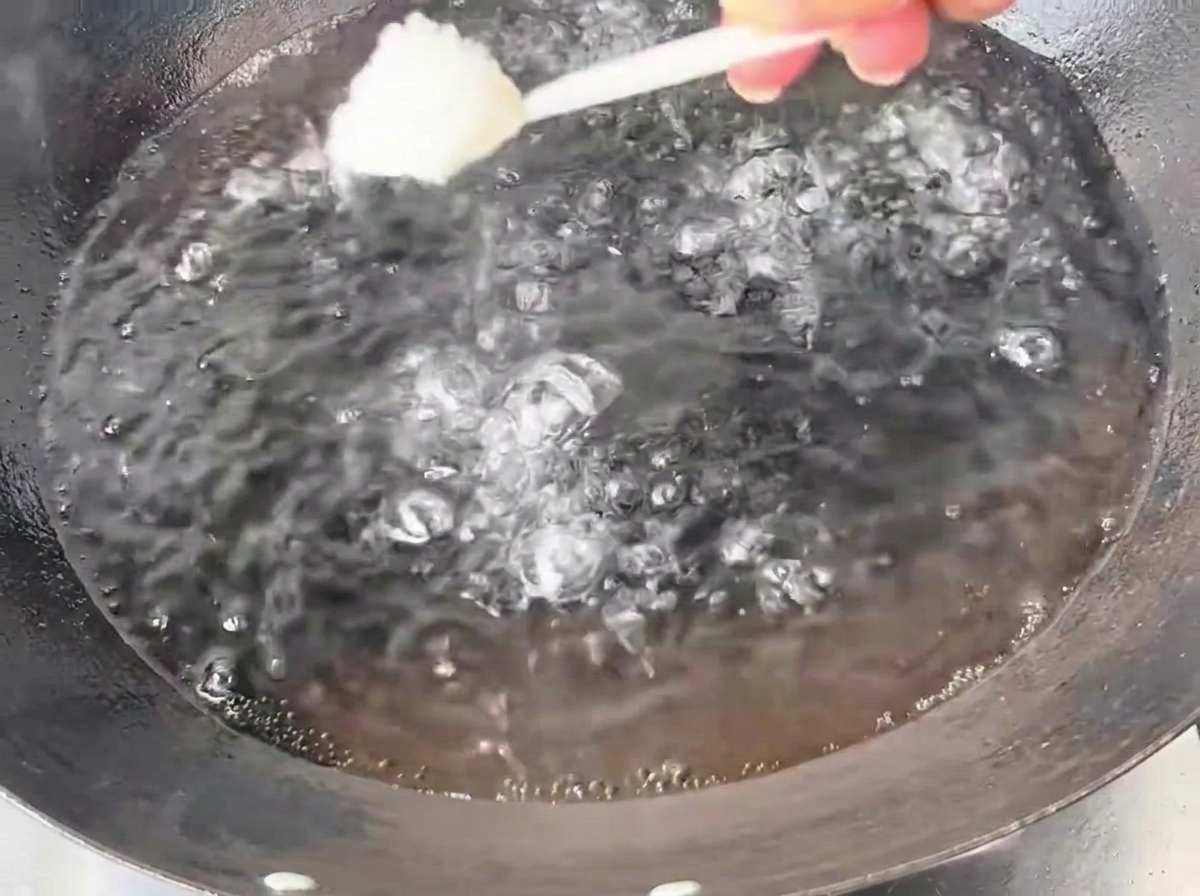Ein Löffel weißes Salz wird in einen großen Eisenwok mit sprudelnd kochendem Wasser gegeben.