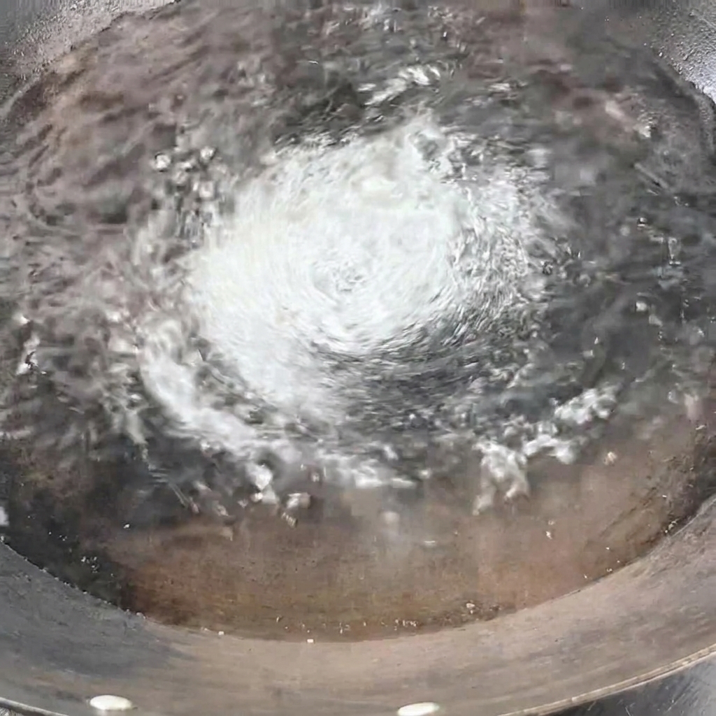 Ein Bündel trockener gelber Spaghetti wird senkrecht in das kochende Wasser im Wok getaucht.