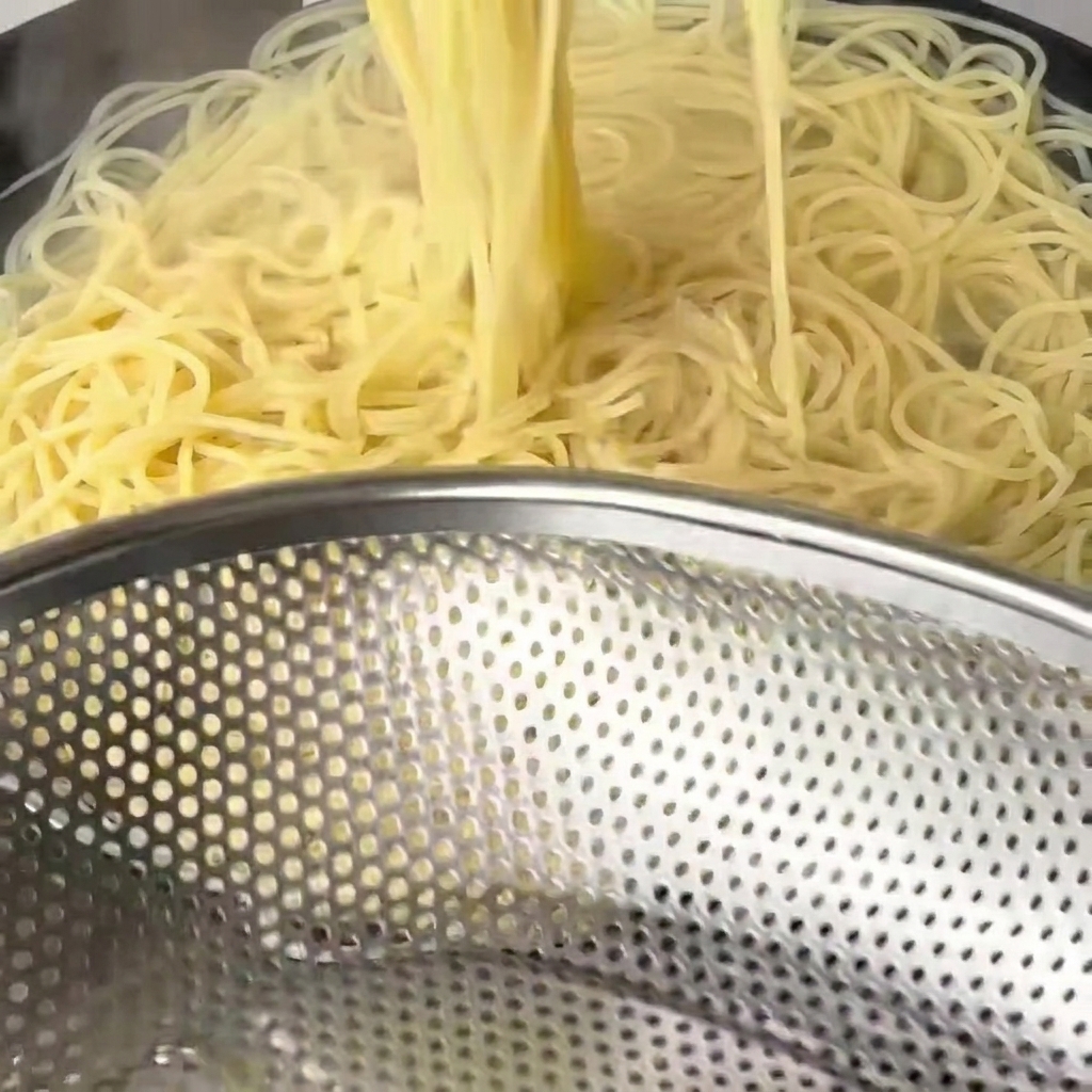 Gekochte, weiche Spaghetti-Nudeln werden mit langen Holzstäbchen aus dem Wasser gehoben.