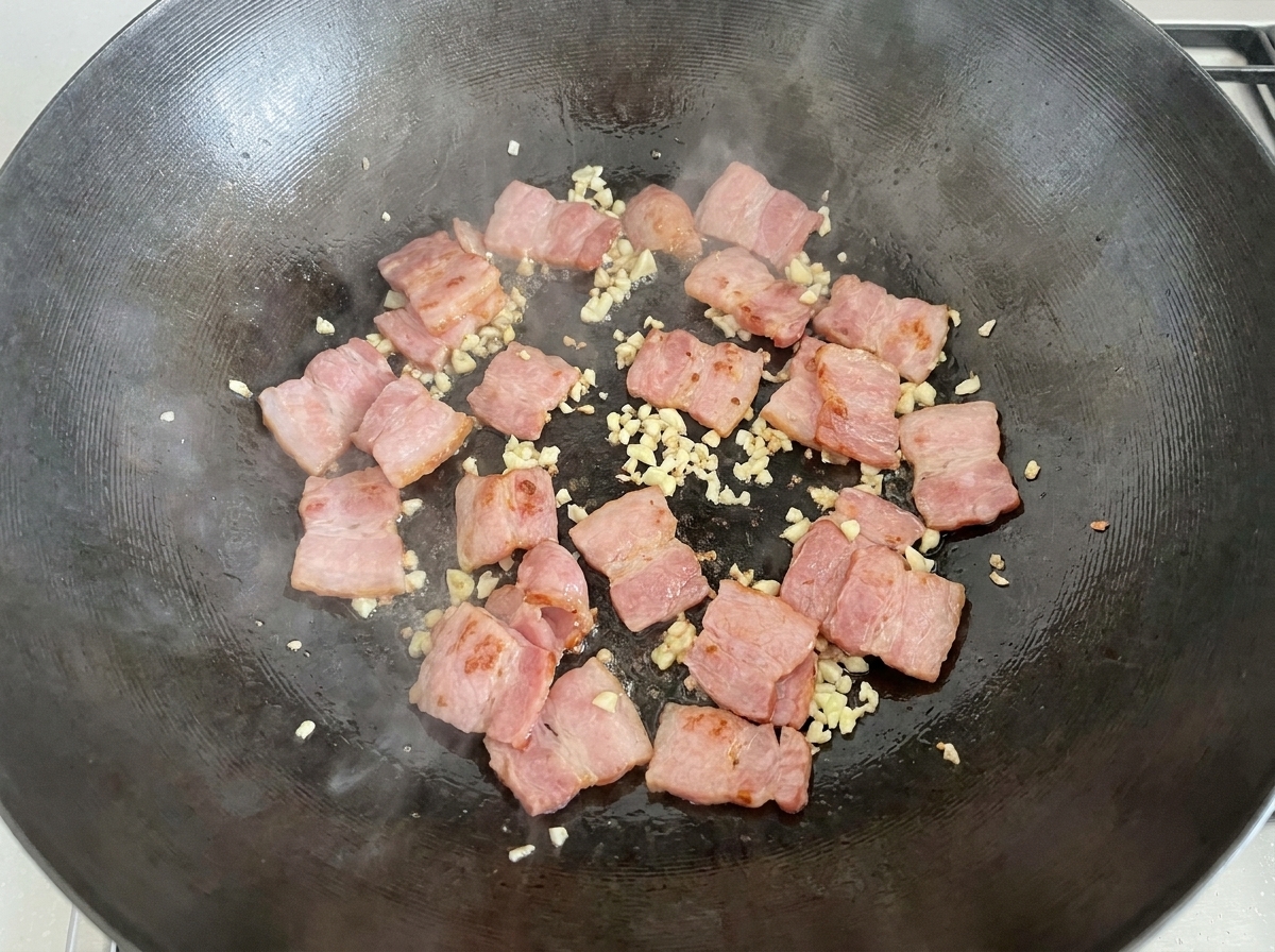 Geschnittene rohe weiße Champignons werden zur Speck-Knoblauch-Mischung in den Wok geschüttet.