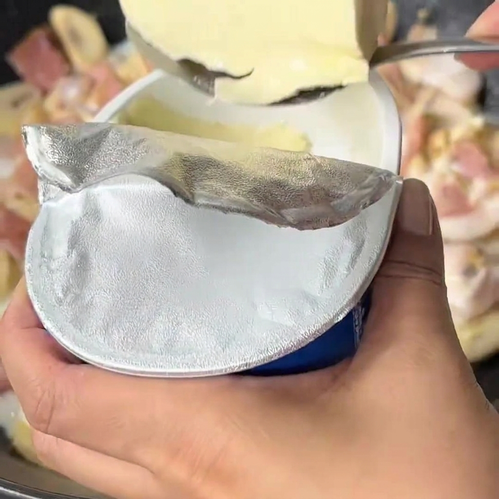 Frischkäse wird in die blubbernde Milch-Gemüse-Sauce in einem Wok gegeben.
