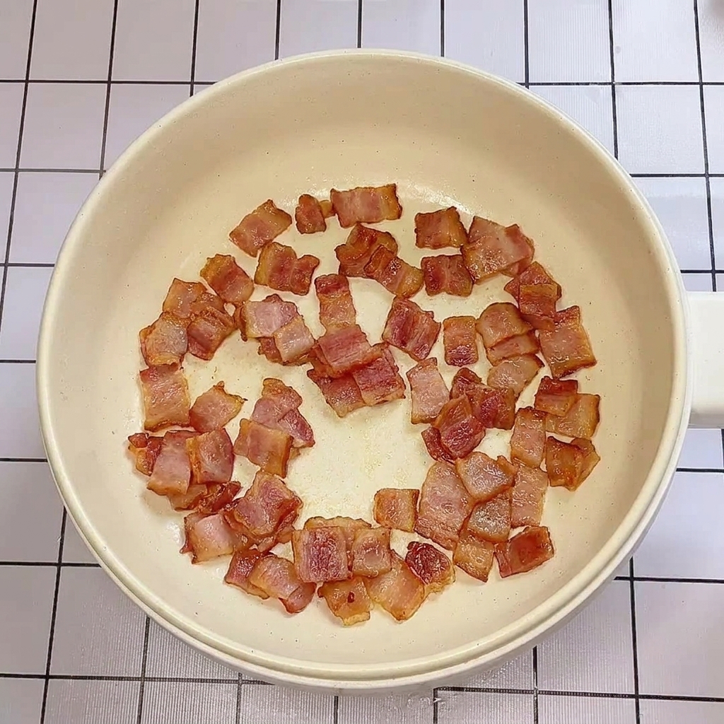 Knuspriger Speck brutzelt in einer flachen Pfanne.