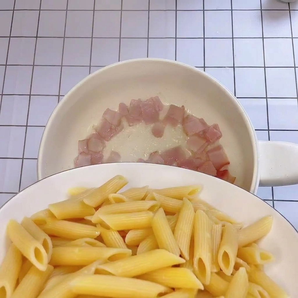 Frisch gekochte Penne werden in die Pfanne zum Speck gegeben.