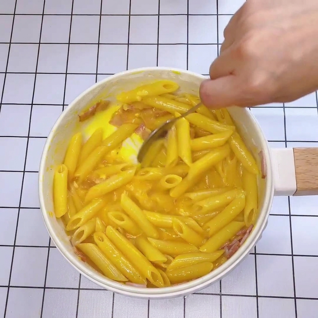 Nahaufnahme beim Rühren, wie die Sauce die Nudeln cremig umschließt.