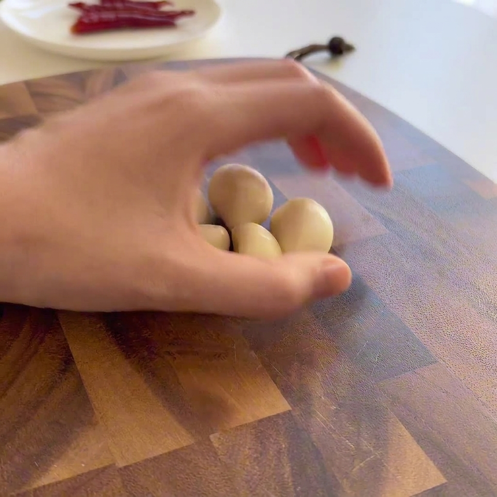 Grob in Scheiben geschnittene Knoblauchzehen auf einem Holzbrett neben einem silbernen Messer.