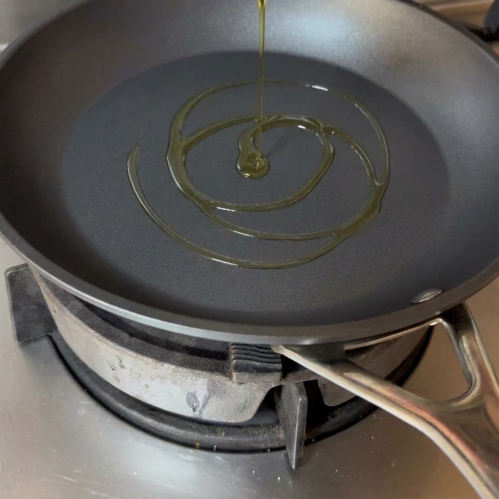Ein Schwung goldenes Olivenöl in einer schwarzen Pfanne.