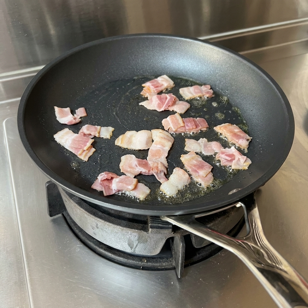 Speckstreifen braten in Öl in einer Pfanne und werden mit einem roten Pfannenwender bewegt.