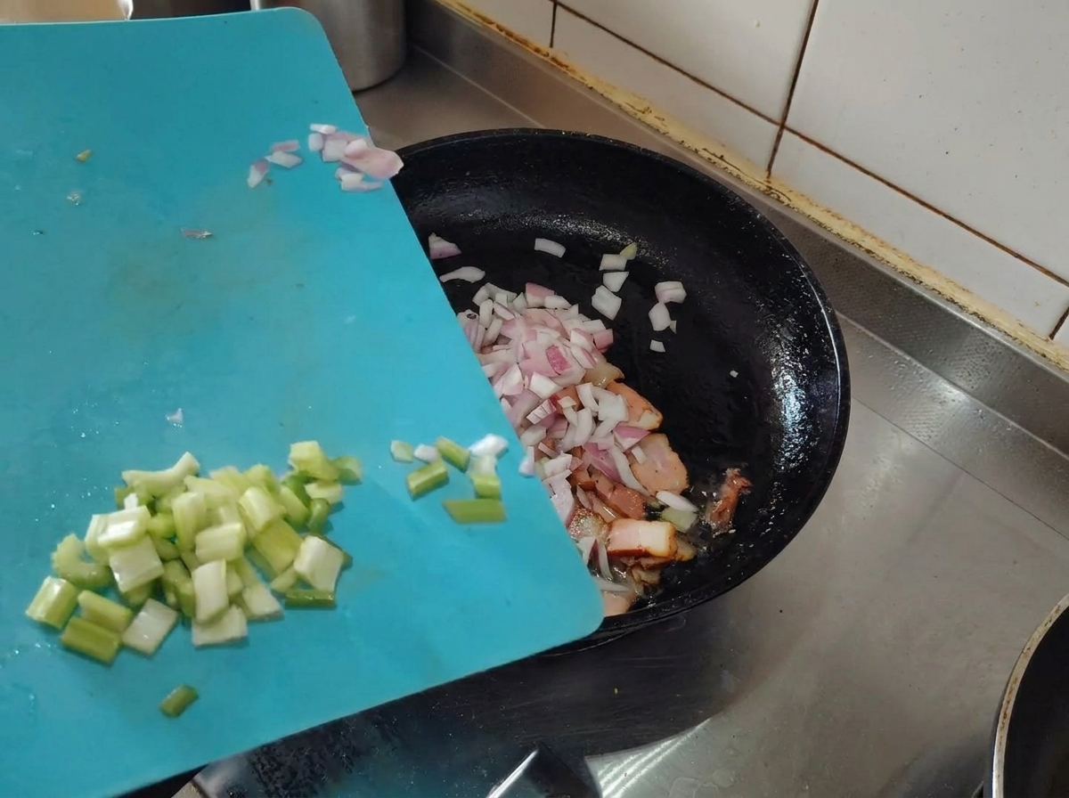 Gehackte Schalotten und Sellerie werden zum gebräunten Speck in die Pfanne gegeben.