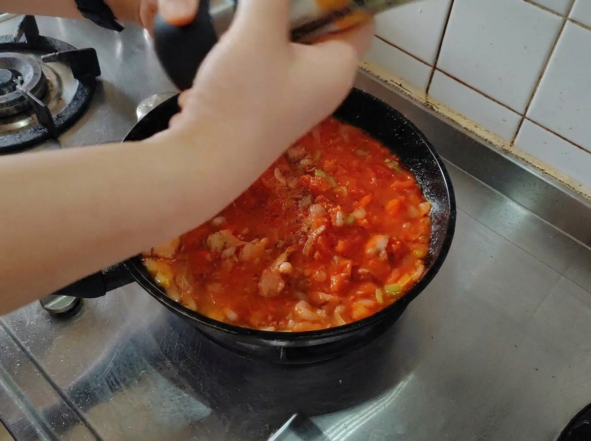 Frisch gemahlener schwarzer Pfeffer wird über die köchelnde Tomaten-Speck-Sauce gestreut.