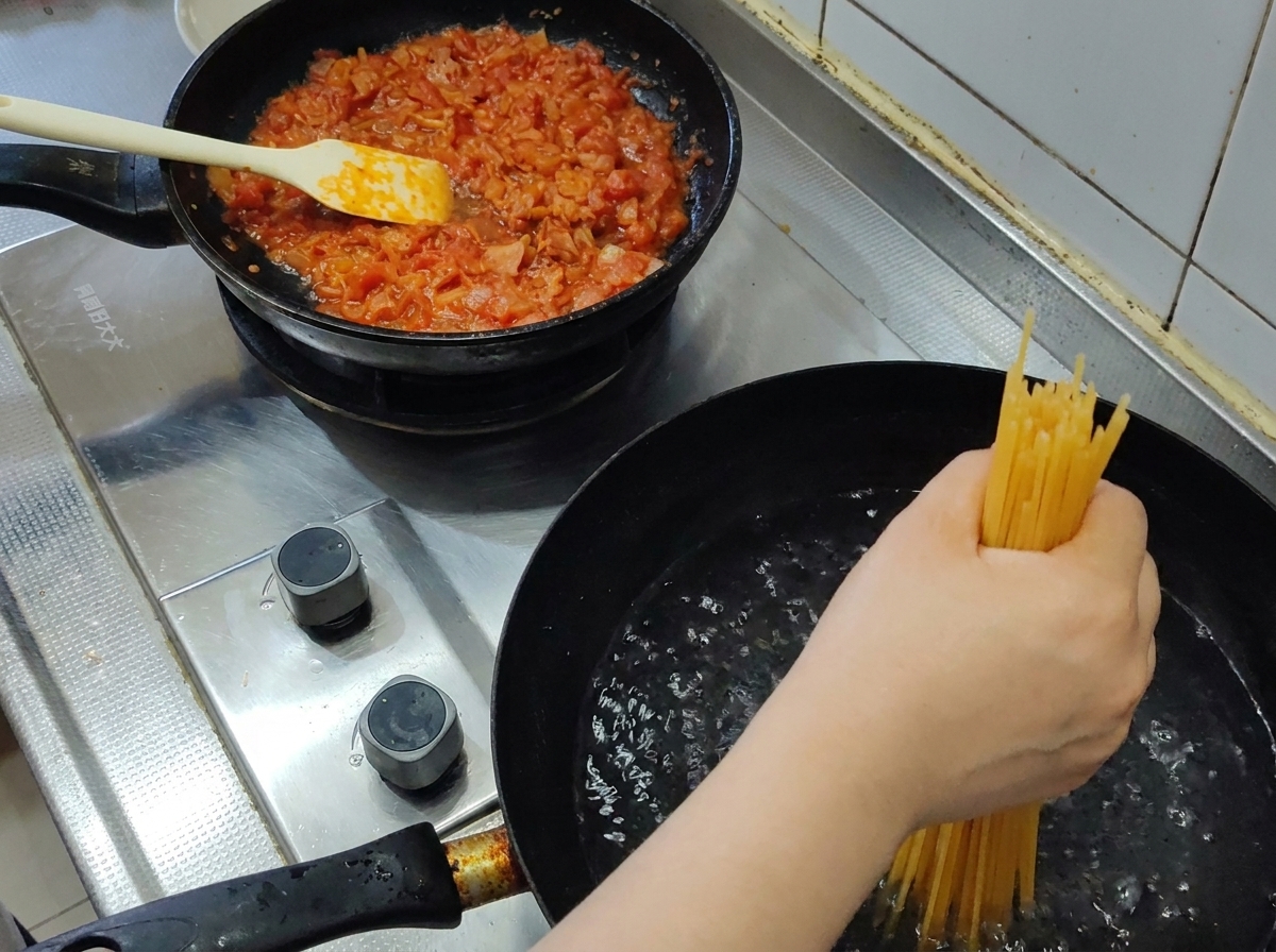 Eine Handvoll Spaghetti wird in einen Topf mit sprudelnd kochendem Wasser gegeben.