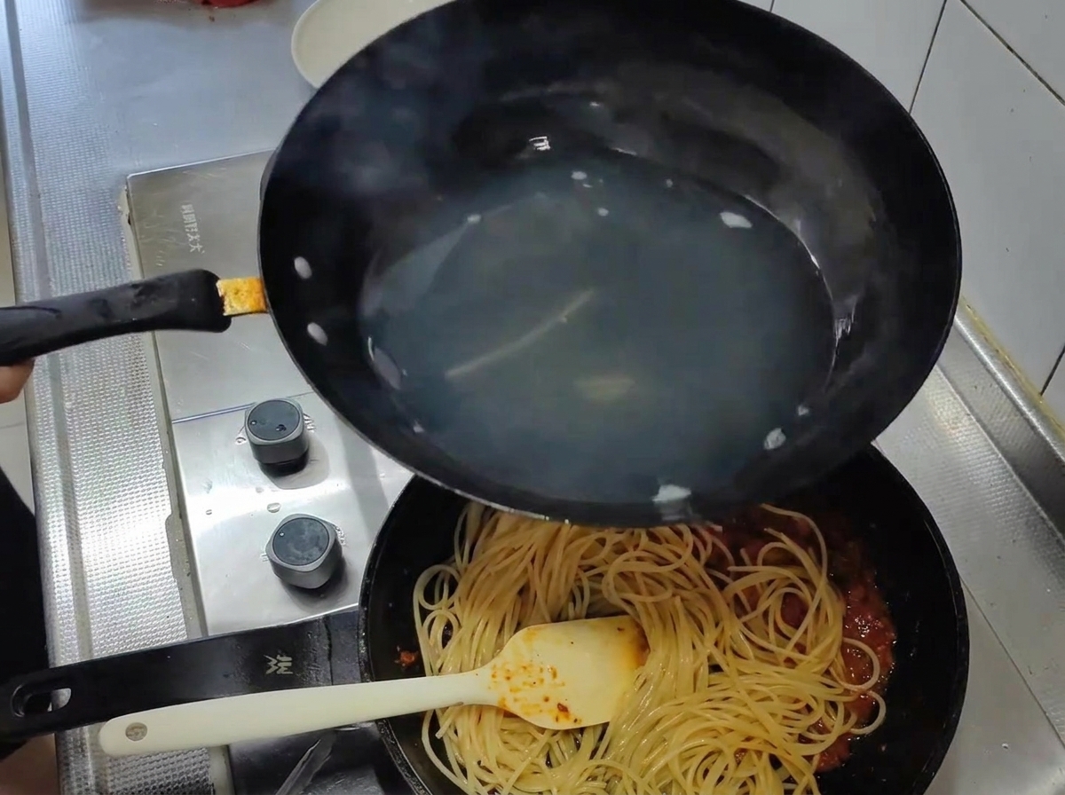 Gekochte Spaghetti werden direkt in die Pfanne mit der Tomatensauce umgefüllt.