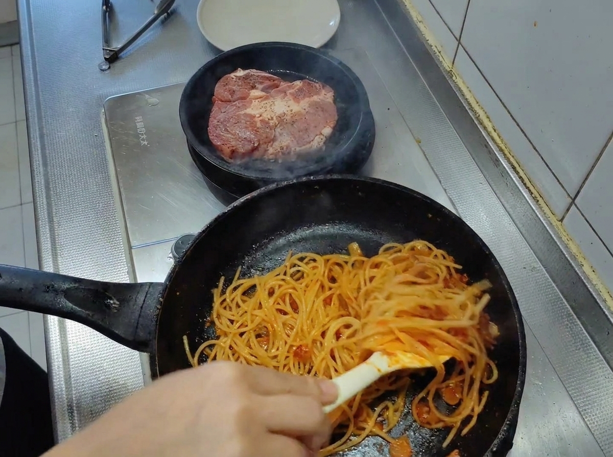 Spaghetti werden mit einer Zange in der Pfanne geschwenkt und mit einer leuchtend roten Tomatensauce überzogen.