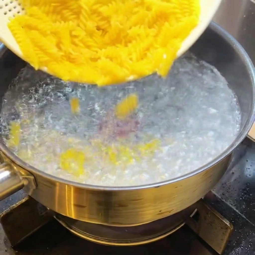 Trockene Fusilli werden in kochendes Wasser gegeben.