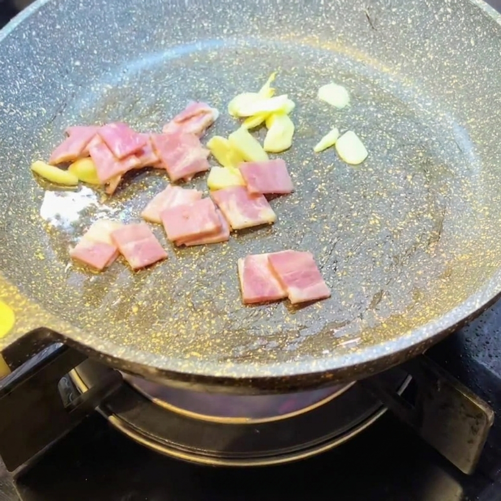 Gewürfelter Speck brät zusammen mit Knoblauch in der Pfanne.