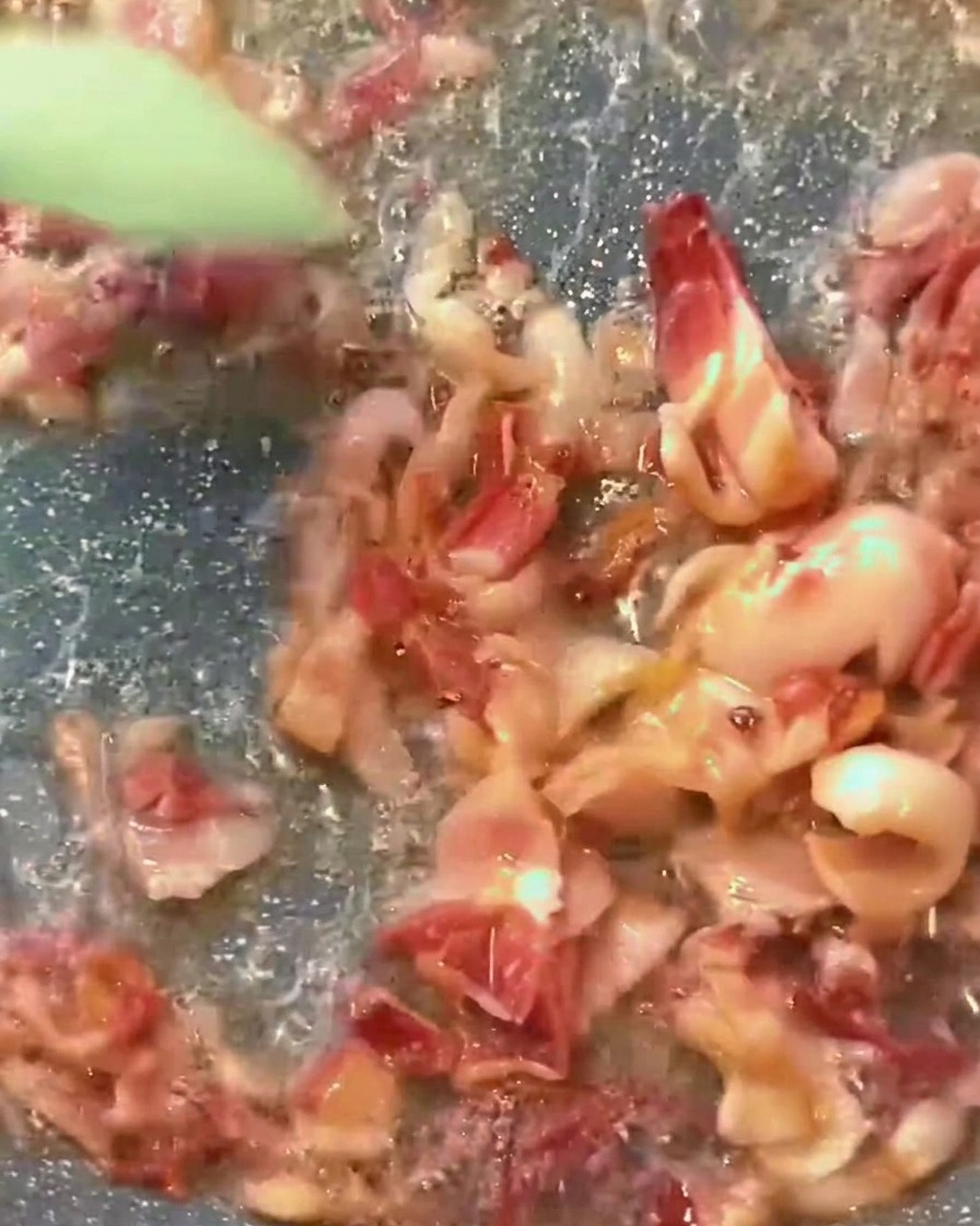 Sämige rote Tomatensauce blubbert in einer Pfanne zusammen mit goldbraunen Speckwürfeln.