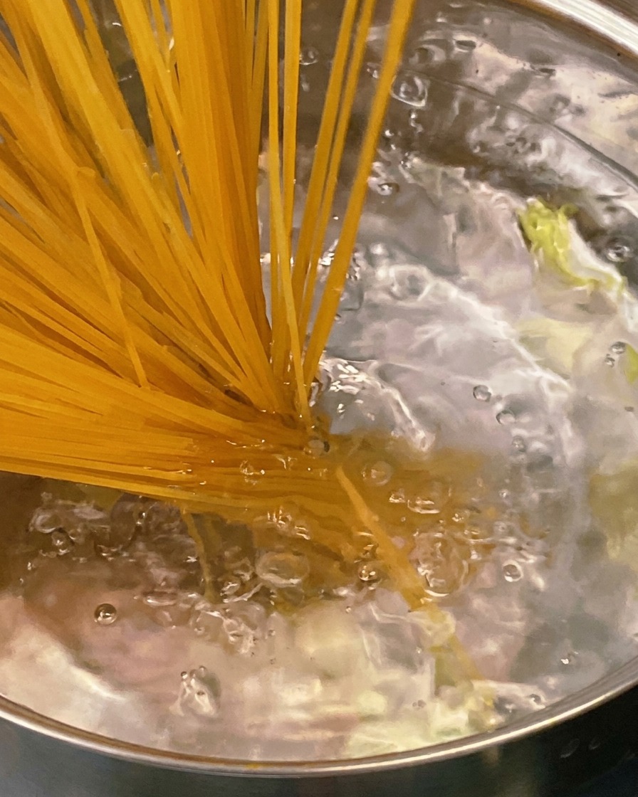 Ein Holzlöffel rührt eine dickflüssige, würzige Tomaten-Speck-Sauce in einer Edelstahlpfanne um.
