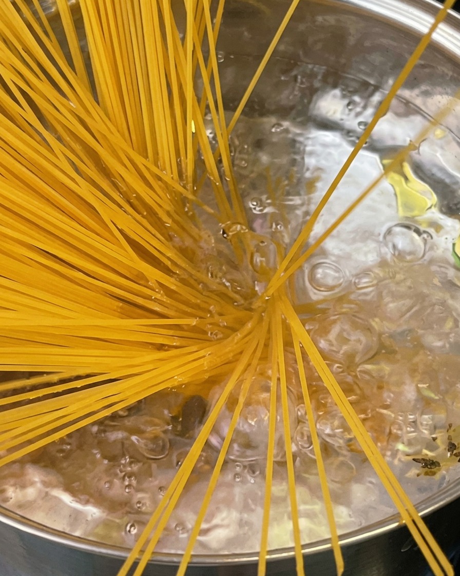 Al dente gekochte Pasta wird mit einer Spaghettizange aus einem Topf gehoben, wobei Dampf aufsteigt.