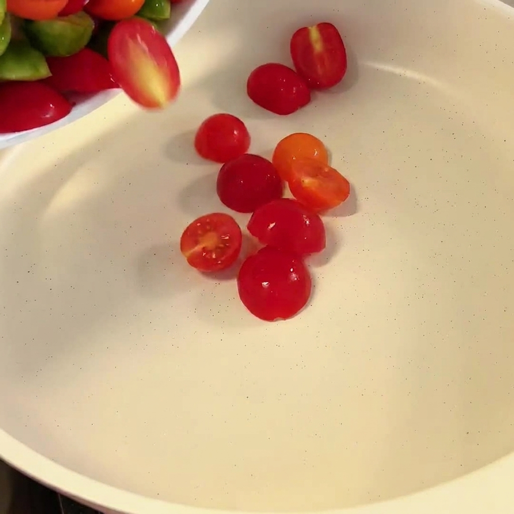 Halbierte rote und grüne Kirschtomaten fallen in eine weiße Pfanne.