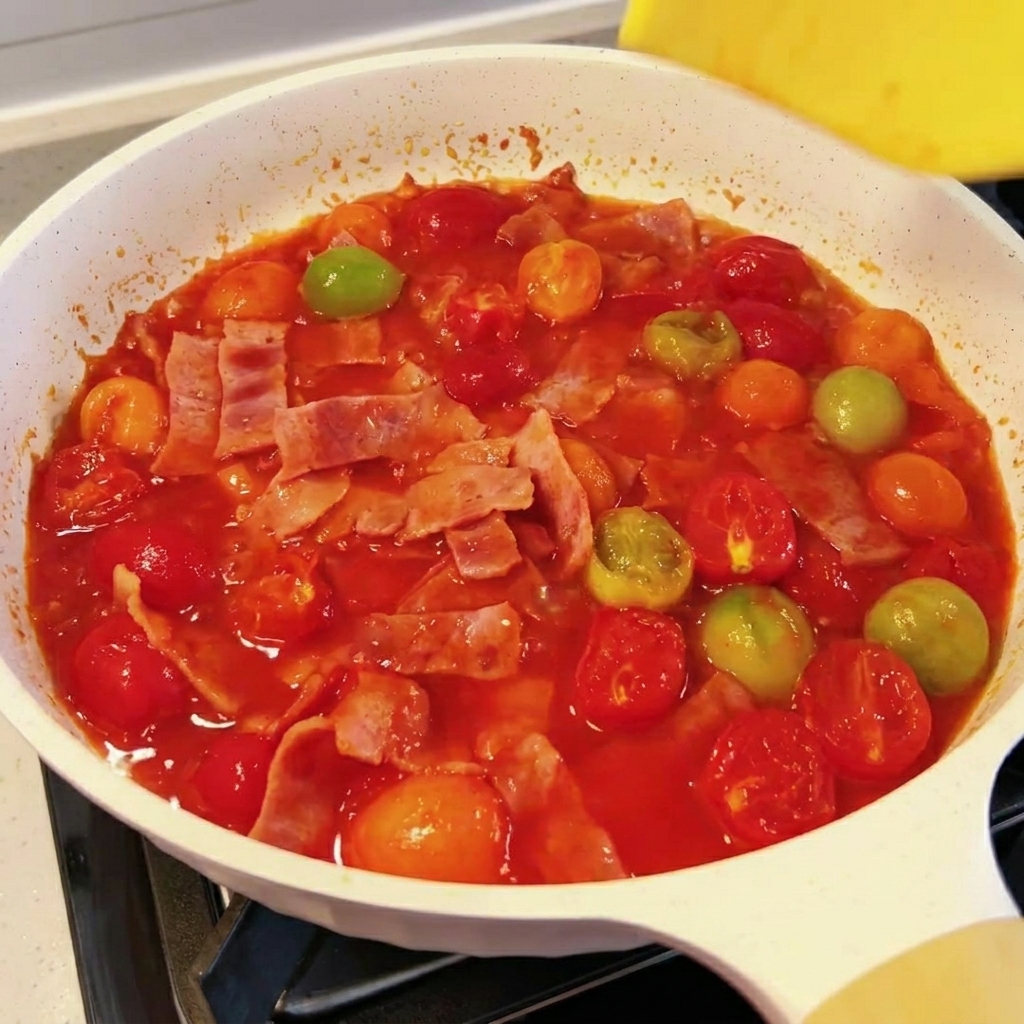 Eine Scheibe Käse schmilzt in einer köchelnden Tomaten-Speck-Sauce.